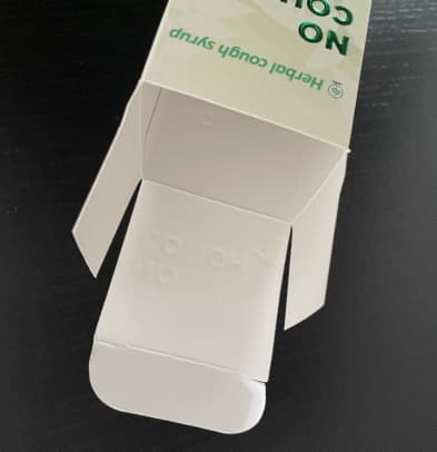 Kotak kemasan produk CBD berwarna putih terbuka di meja, menunjukkan tempat untuk produk cair.